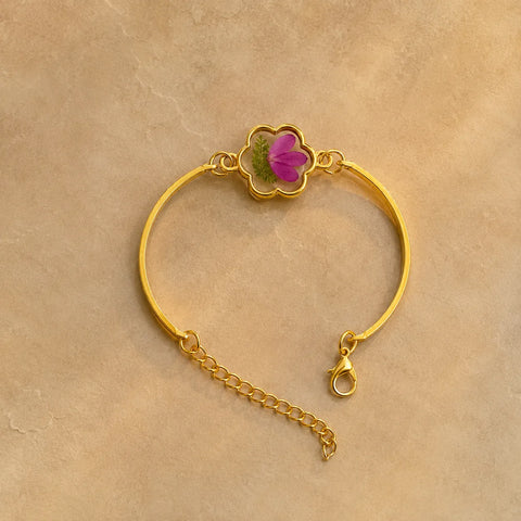 Gold bracelet with a pink flower charm on a beige background