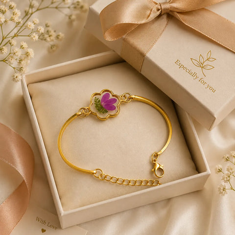Gold bracelet with floral design in a gift box, surrounded by flowers and ribbons.