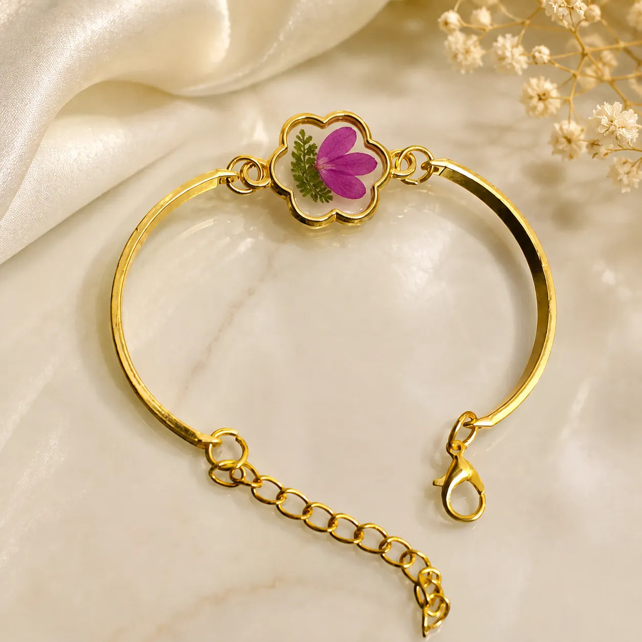 Gold bracelet with a floral charm on a soft beige background
