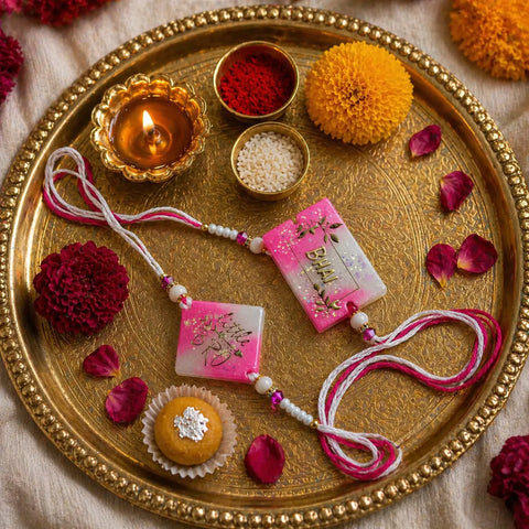 Decorative tray with pink pouches, flowers, and a lit candle on a textured surface.