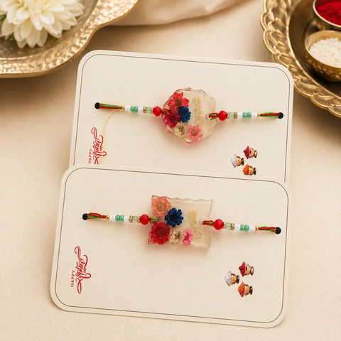 Two floral-themed Rakhi (Hindu religious thread) on a card with 'Happy Rakhi' text, placed on a beige surface.