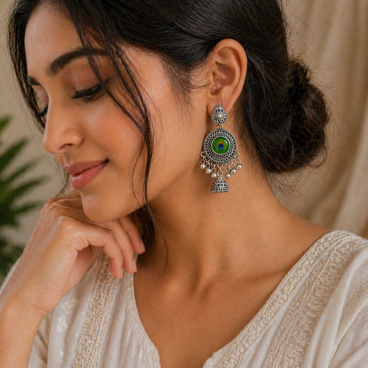 Woman wearing a decorative earring with a green gemstone, set against a neutral background.