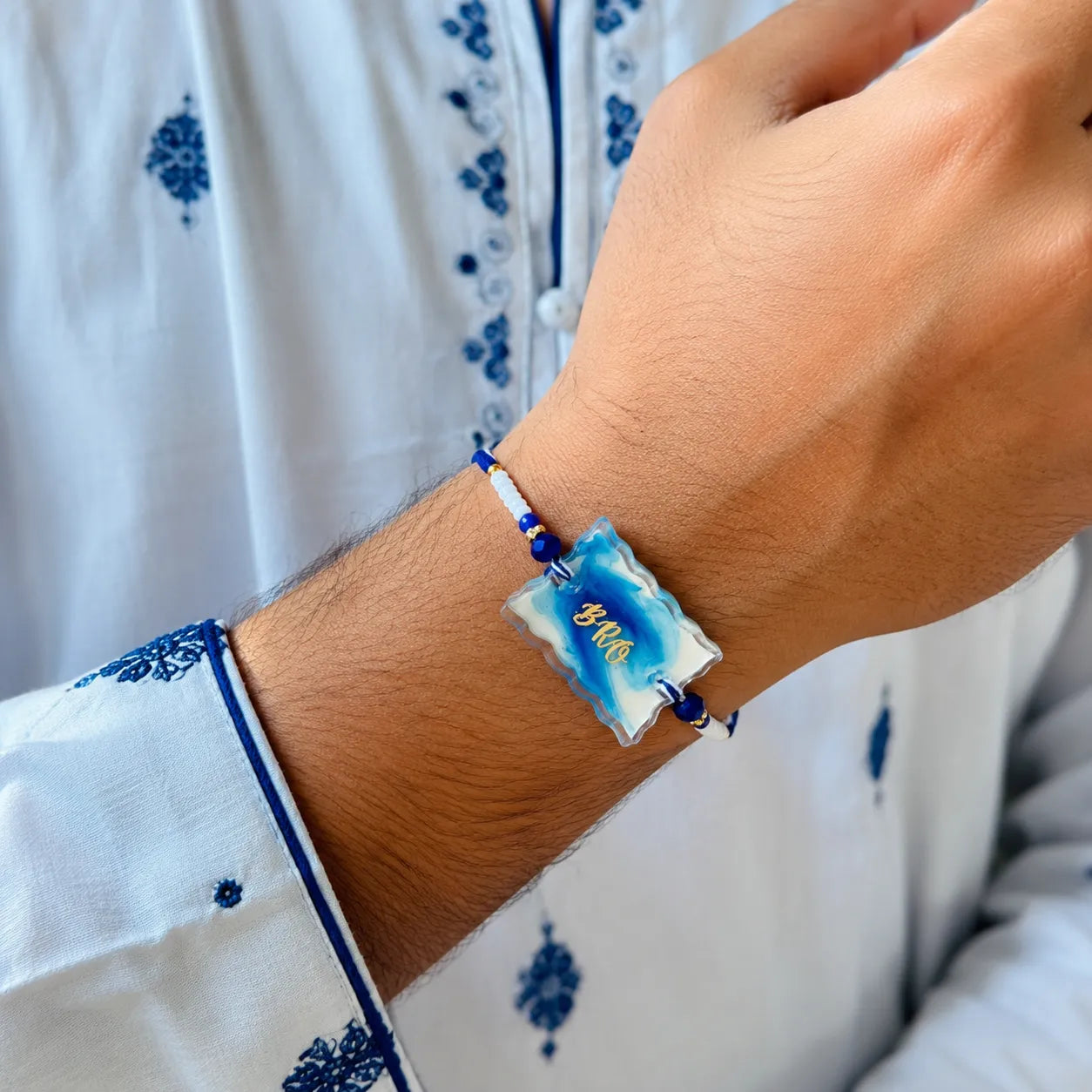 Hand wearing a blue and white bracelet with a decorative design on a white garment with blue patterns.