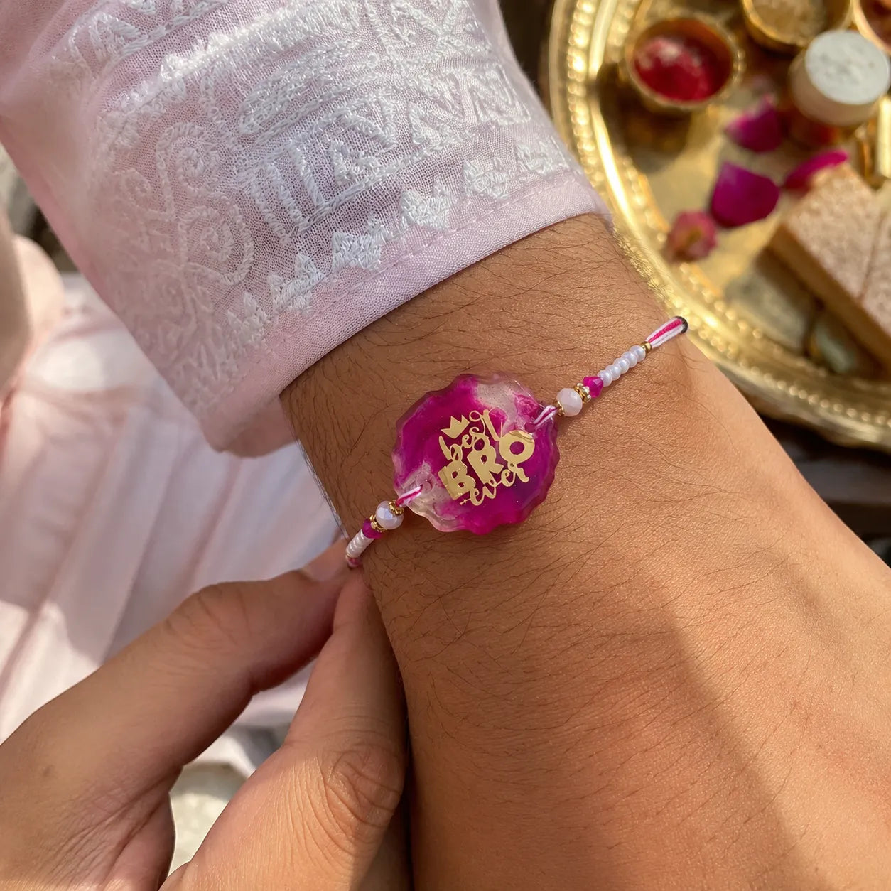 Close-up of a wrist wearing a pink bracelet with gold accents, held by a hand.