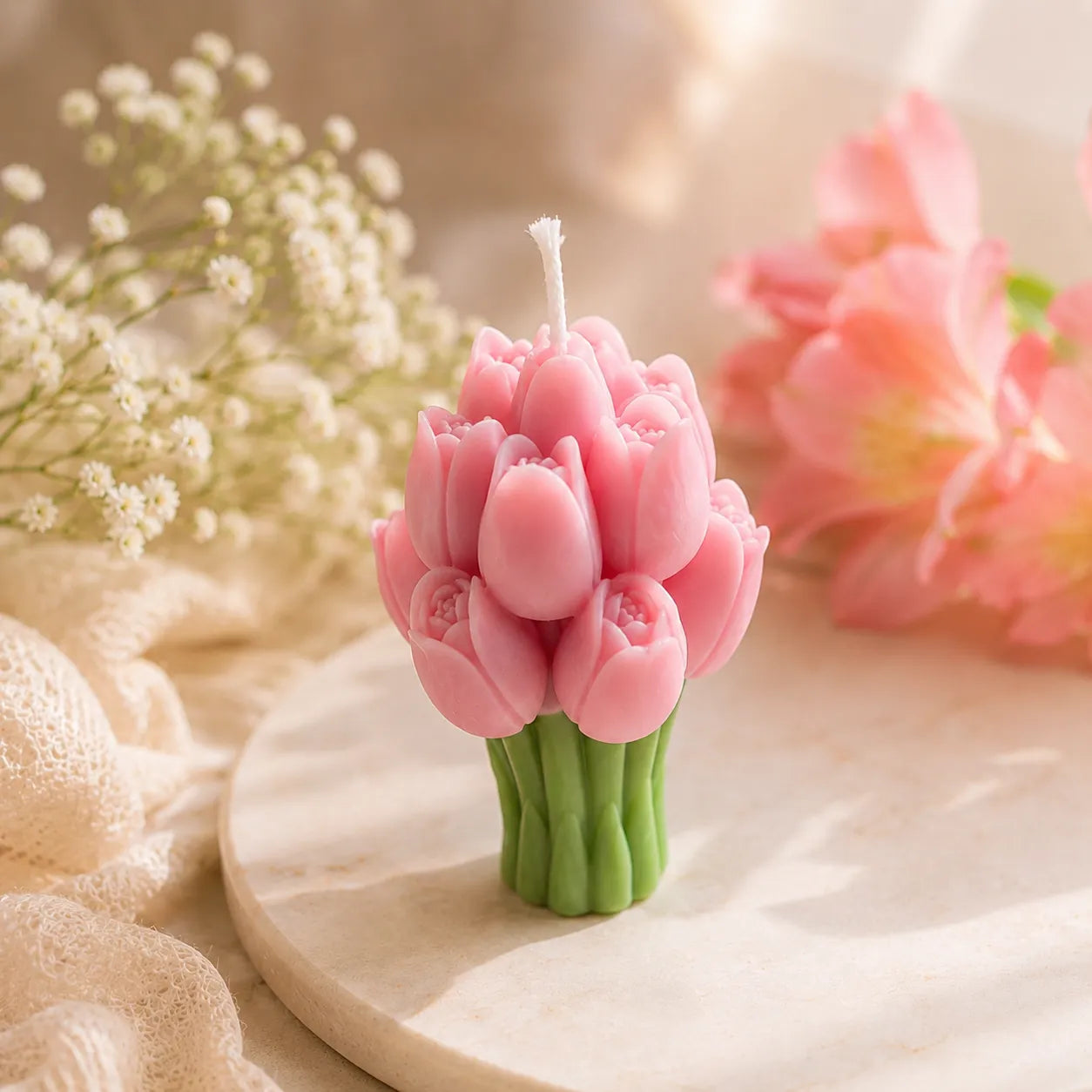 Pink tulip-shaped candle on a wooden surface with flowers in the background