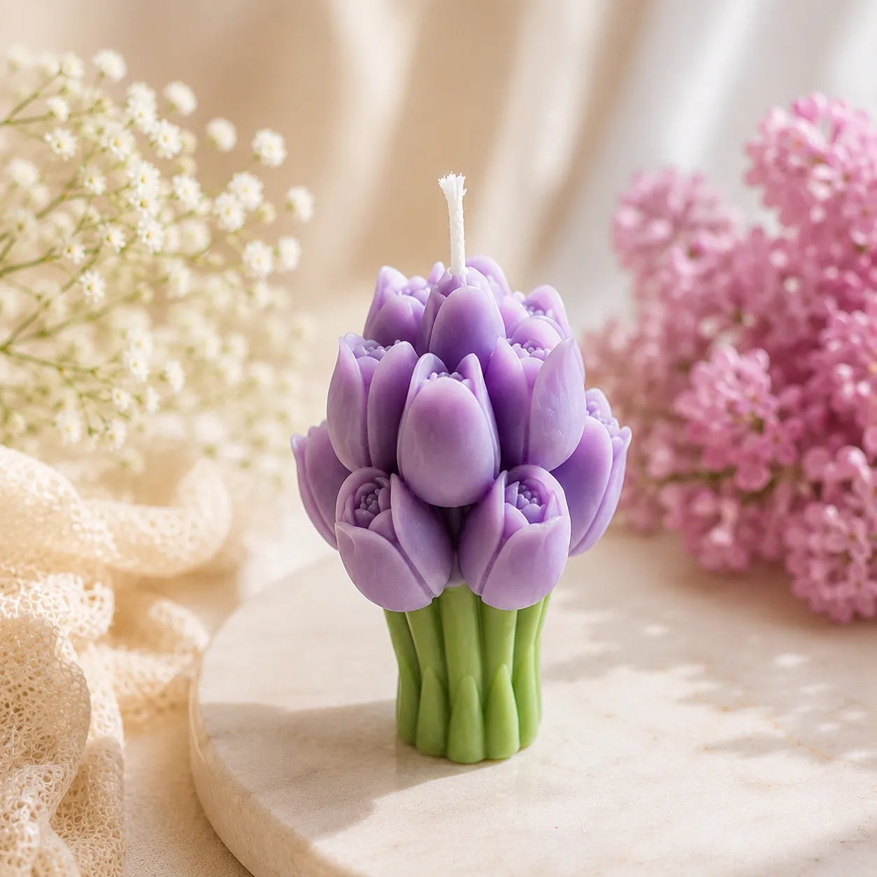 Purple flower-shaped candle on a wooden surface with flowers in the background