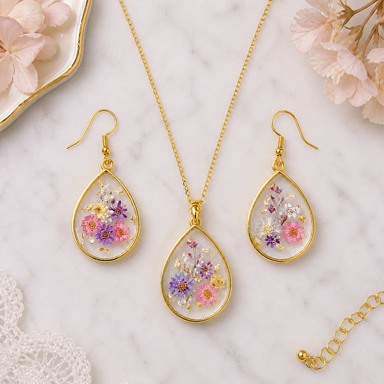 Jewelry set with floral teardrop pendants and earrings on a marble surface.