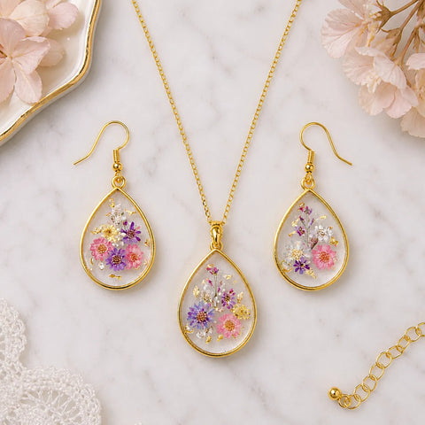 Jewelry set with floral teardrop pendants and earrings on a marble surface.