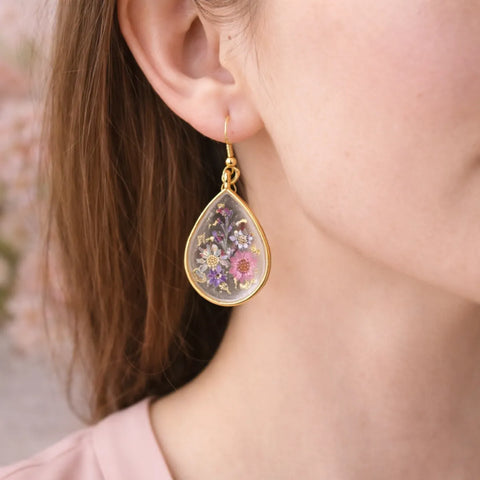 Teardrop-shaped earrings with floral design worn by a person