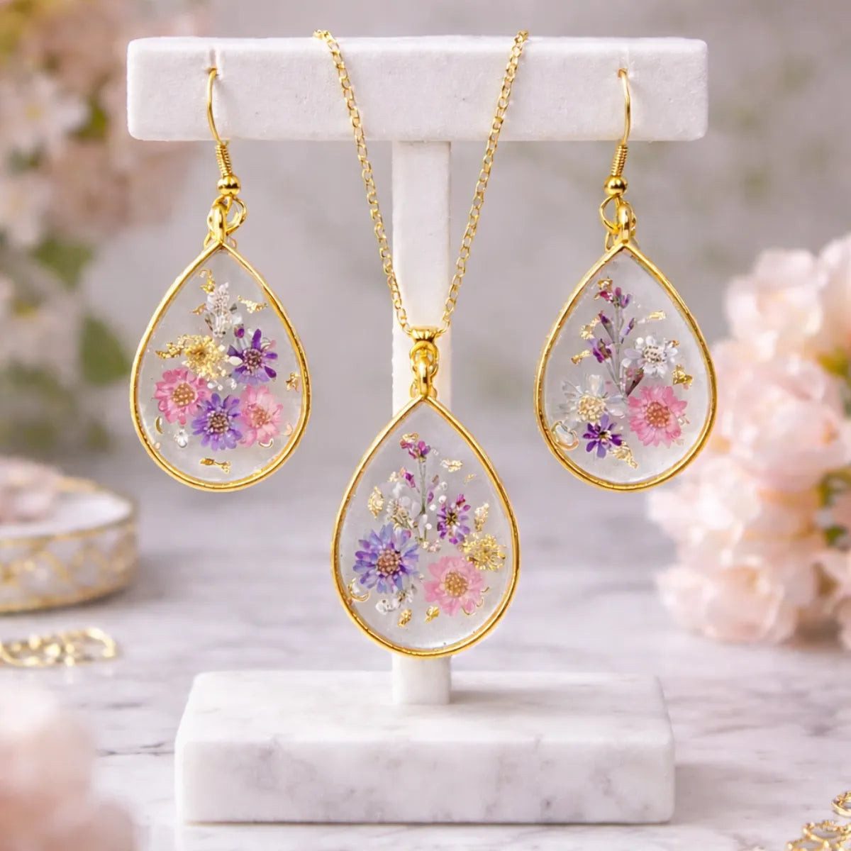 Gold-framed earrings and necklace with floral designs on a marble stand.