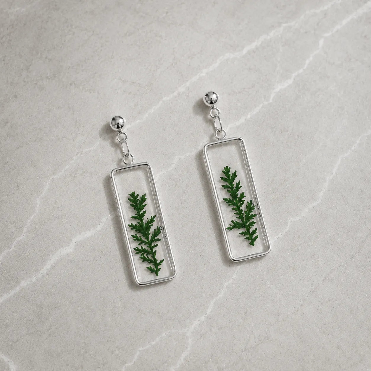 Rectangular earrings with green leafy design on a light gray surface