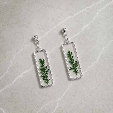 Rectangular earrings with green leafy design on a light gray surface