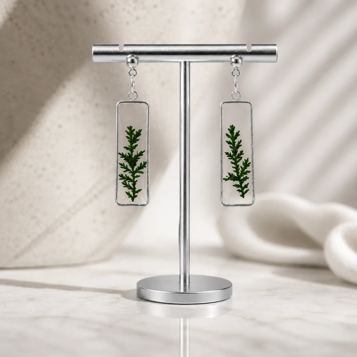 Earrings with green leaf design on a stand against a neutral background