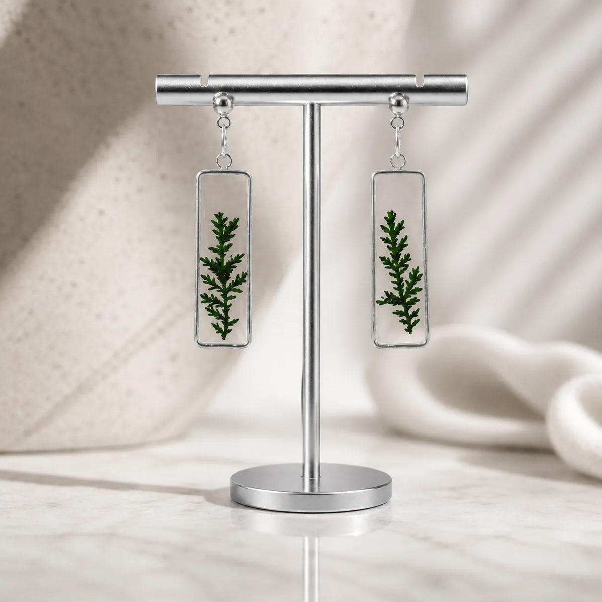 Earrings with green leaf design on a stand against a neutral background