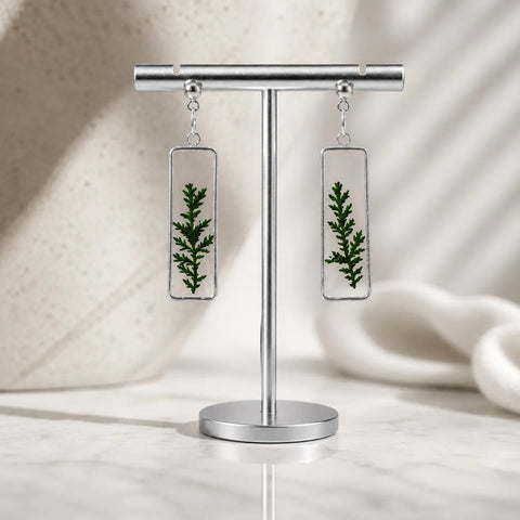 Earrings with green leaf design on a stand against a neutral background