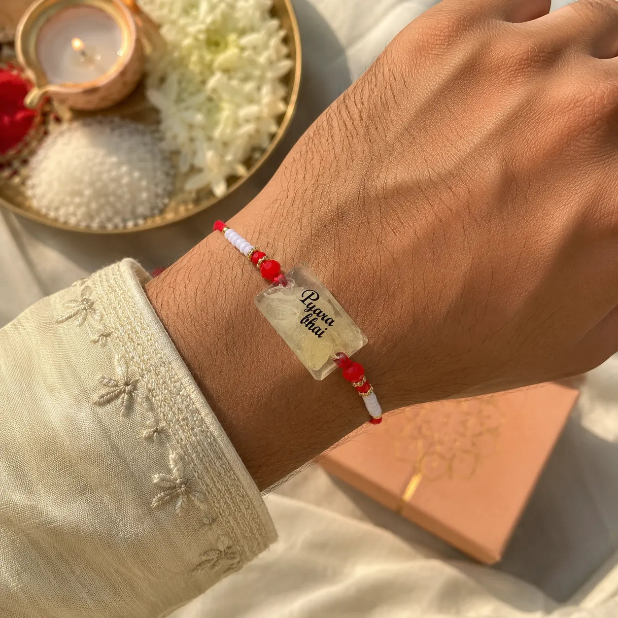 Hand wearing a red and white beaded bracelet with a clear tag, set against a soft focus background.