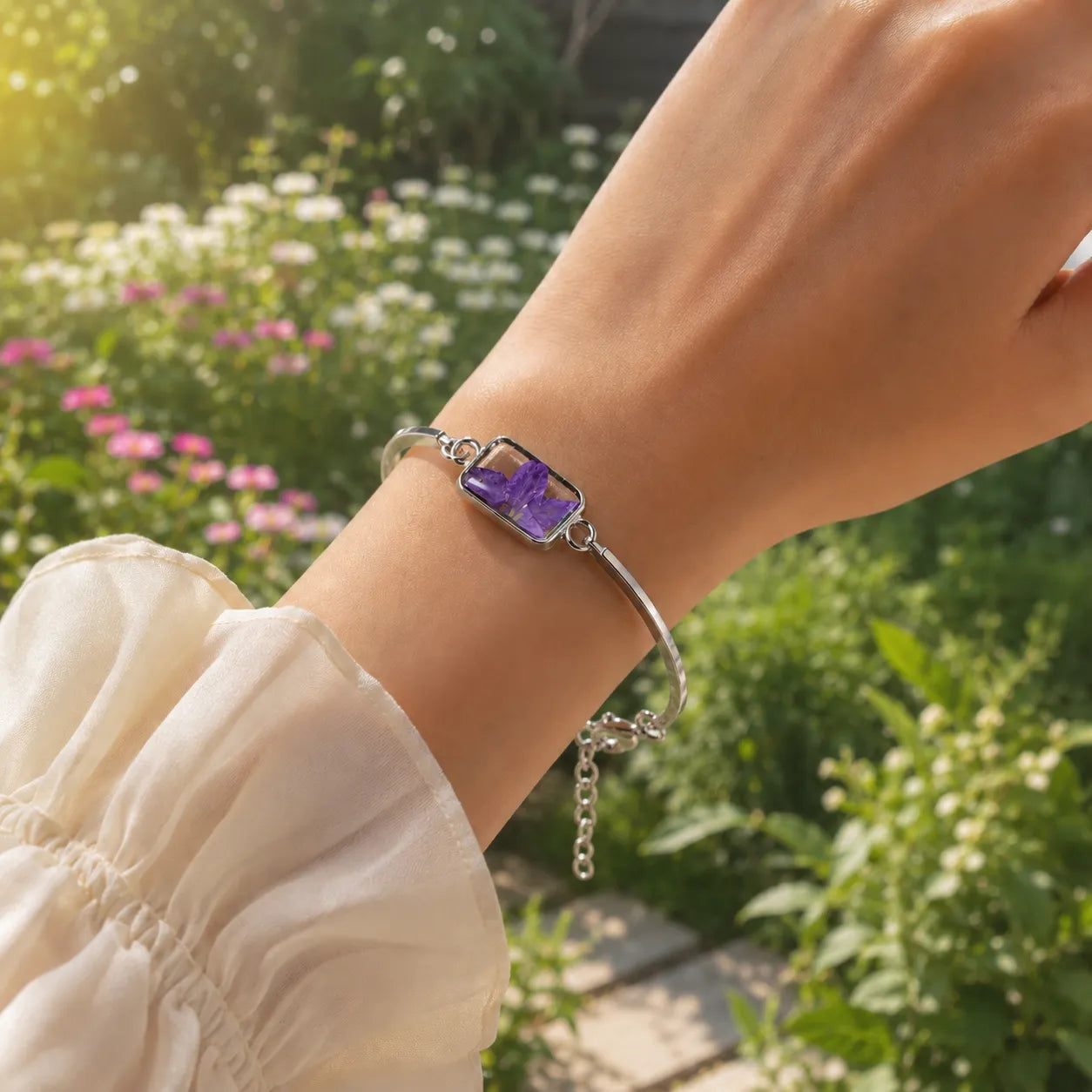 Hand wearing a silver bracelet with a purple stone in front of a garden background