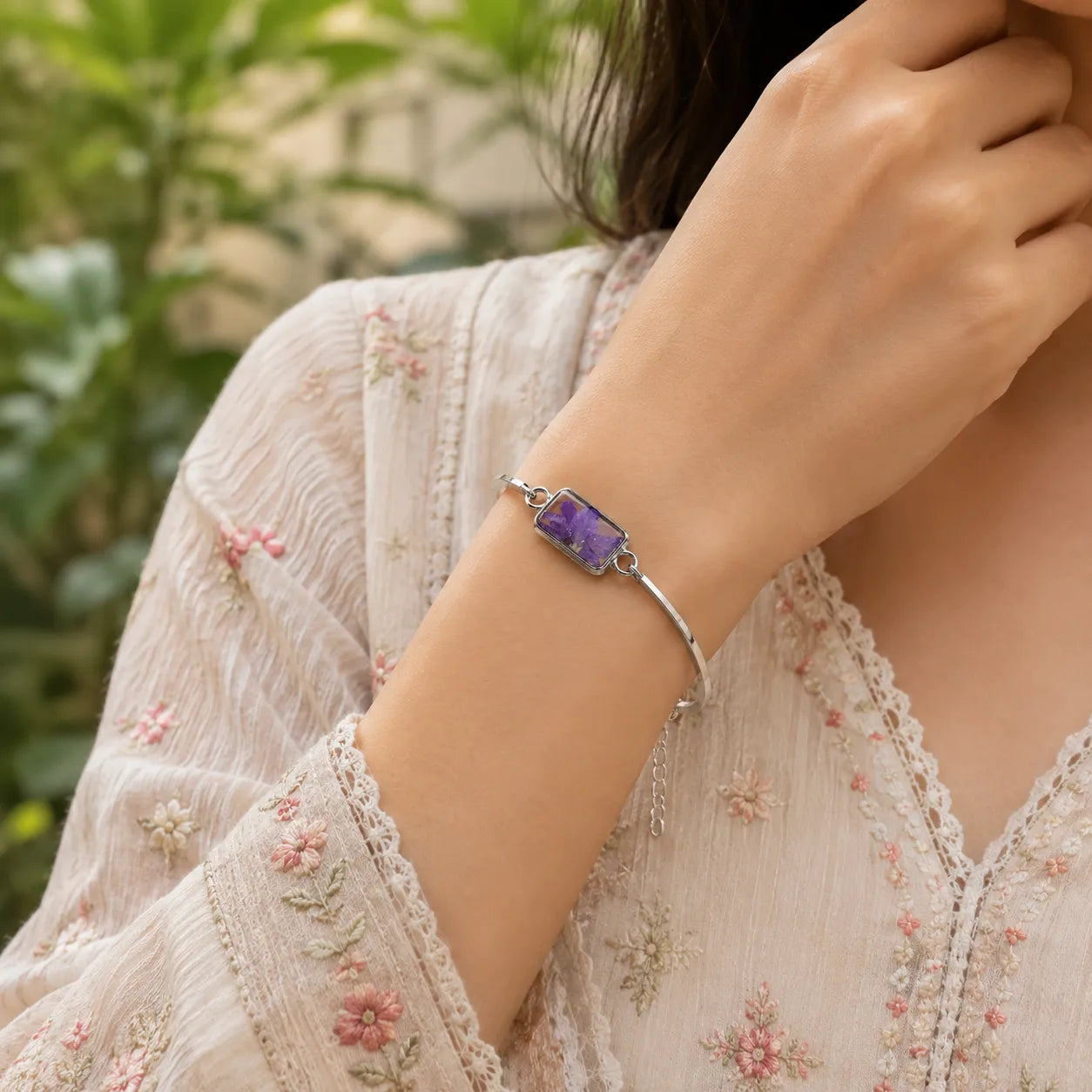 Woman wearing a silver bracelet with a purple gemstone against a blurred natural background