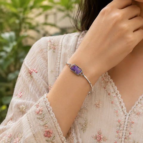 Woman wearing a silver bracelet with a purple gemstone against a blurred natural background
