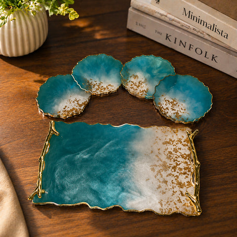 Set of blue and gold coasters on a wooden surface with books and a plant in the background.