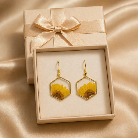 Gold earrings with hexagonal design featuring dried flowers in a beige gift box with a bow.