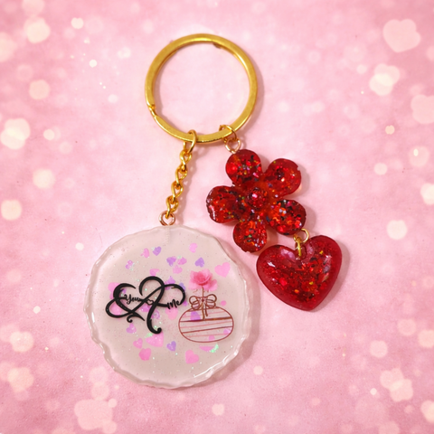 Personalized resin keychain for couples featuring romantic red glitter heart and flower charms with a white "You & Me" circular base.