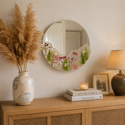 Decorative mirror with floral design on a wooden console table with books, a vase, and a lamp.