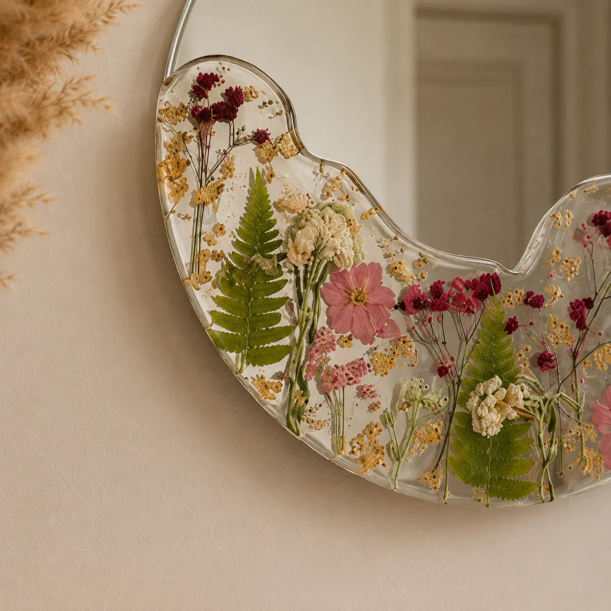 Heart-shaped mirror with pressed flowers and leaves on a beige wall