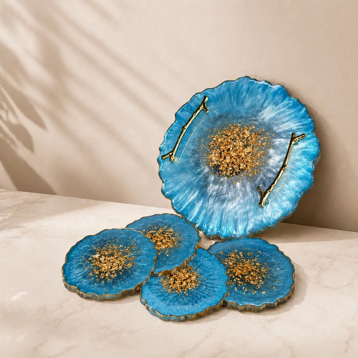 Sky blue resin serving tray with gold handles and matching geode coasters set featuring gold flakes glossy finish on marble surface