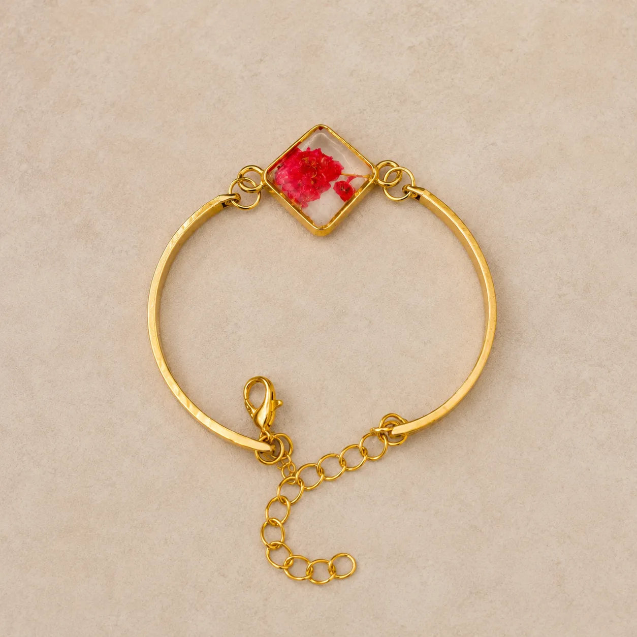 Gold bracelet with a red flower design on a beige background