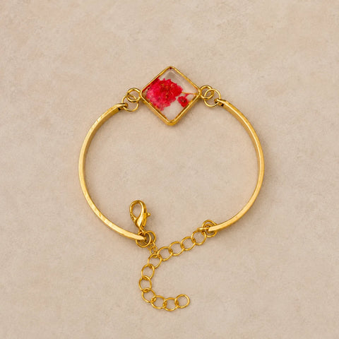 Gold bracelet with a red flower design on a beige background