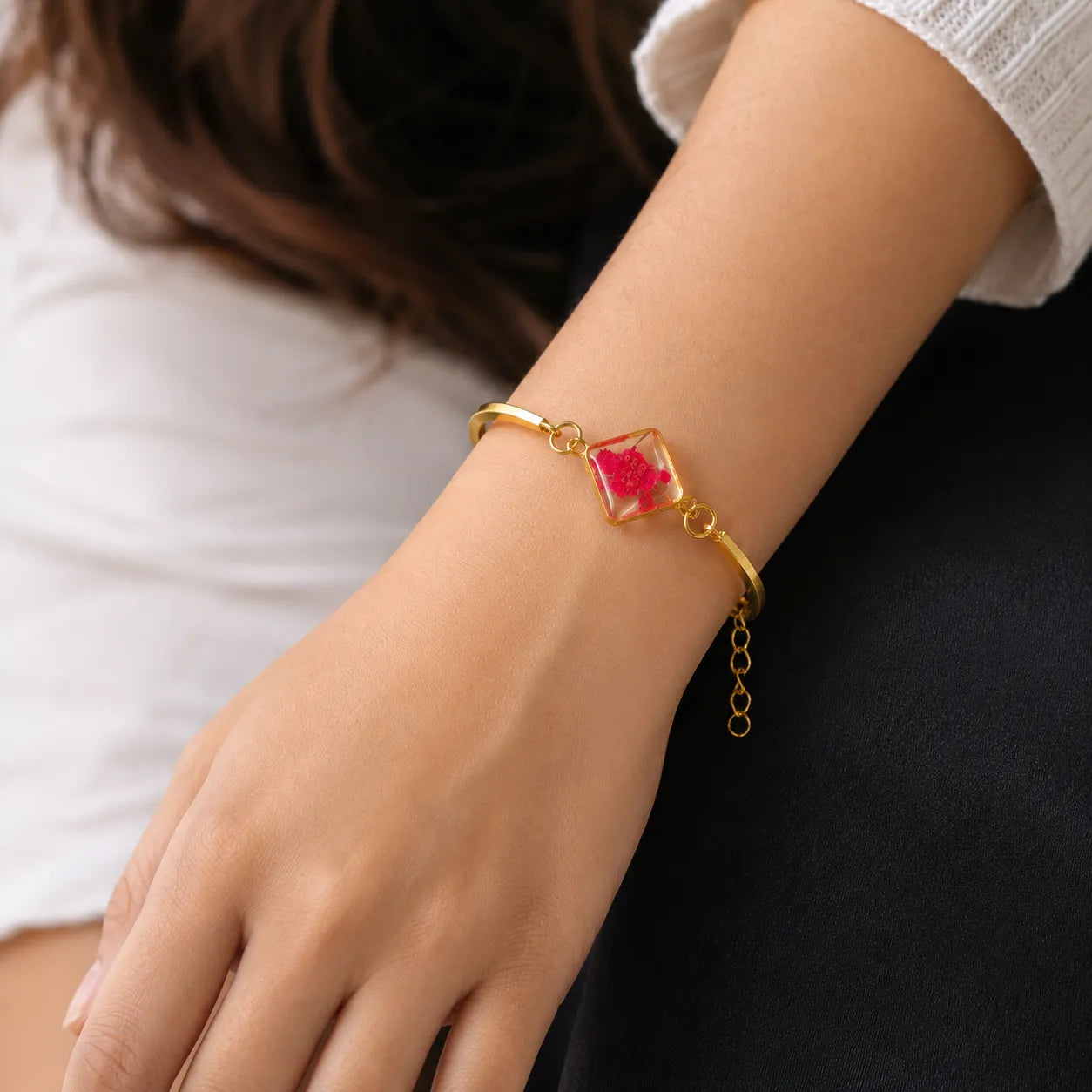 Gold bracelet with a red gemstone on a wrist against a neutral background