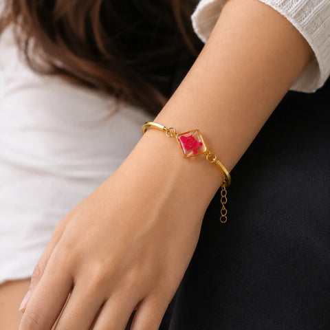 Gold bracelet with a red gemstone on a wrist against a neutral background