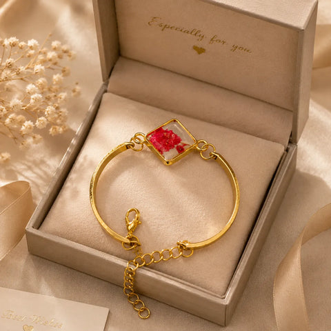Gold bracelet with a red flower charm in an open jewelry box.