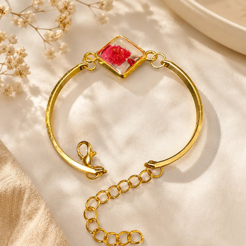 Gold bracelet with a clear heart-shaped charm featuring red flowers on a beige fabric background.