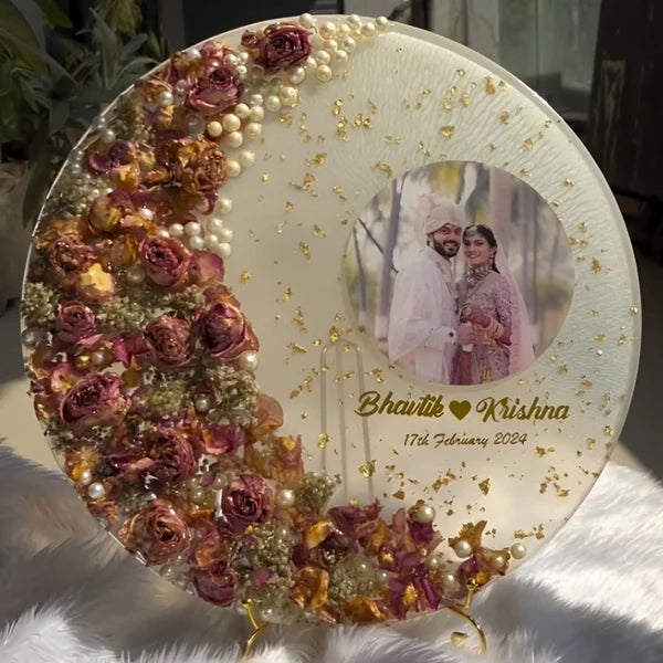 Circular resin preservation frame for wedding varmala flowers with personalized couple photo, golden flakes, and pearl detailing.