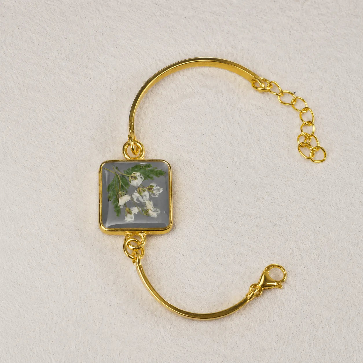 Gold bracelet with a square charm featuring floral design on a light gray background