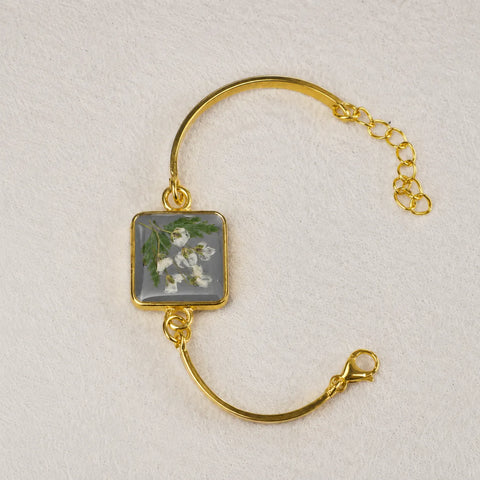 Gold bracelet with a square charm featuring floral design on a light gray background